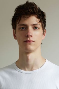 a young man in a white t - shirt looking at the camera