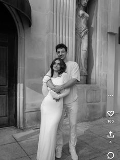 a man and woman standing next to each other in front of a building with statues