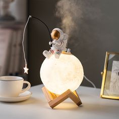 an astronaut is sitting on top of a moon lamp next to a cup and saucer