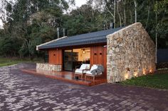 a small house made out of rocks and wood with two white chairs on the porch