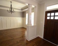 an empty living room with wood floors and white trim on the walls, two chandeliers hanging from the ceiling