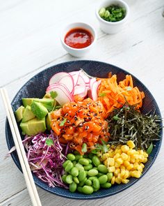 a bowl filled with vegetables and chopsticks on top of a white wooden table