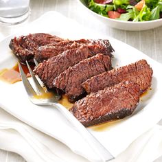 steak on a white plate with a salad in the backgroung and fork