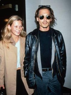 a man and woman standing next to each other in front of a white wall wearing sunglasses