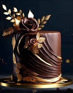 a chocolate cake decorated with gold leaves and flowers on a plate in front of a dark background