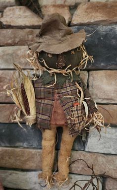 an old fashioned scarecrow with a hat and scarf on it's head, standing next to a brick wall