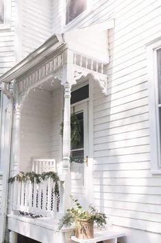 a white house with a bench and potted plants on the front porch, in front of it