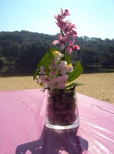 a vase filled with rocks and flowers on top of a pink cloth covered tablecloth