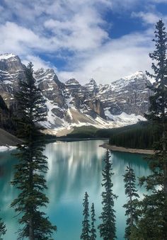 a lake surrounded by snow covered mountains and pine trees in the foreground with blue water