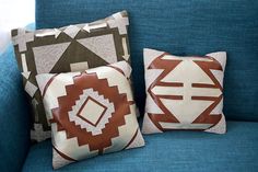 three pillows on a blue couch with brown and white designs in the middle one is square, the other two are rectangleed