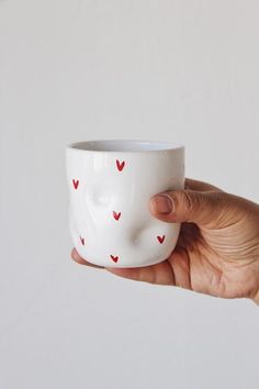 a hand holding a white cup with red hearts on the inside and face drawn on it