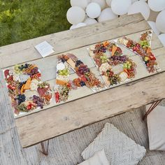 a wooden table topped with lots of different types of food next to white balloons in the background