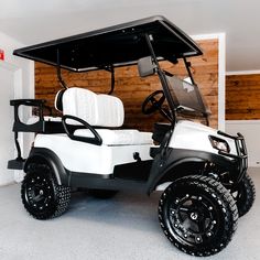 a white and black golf cart parked in a room with wood paneling on the walls