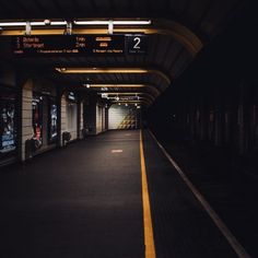 an empty train station at night with no people on the platform and signs above it