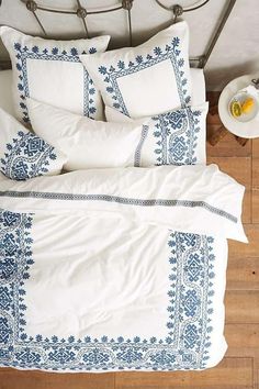 a bed with white and blue comforters on top of it next to a bowl of fruit