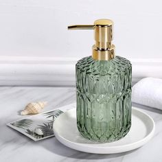 a green glass soap dispenser sitting on a plate next to a towel