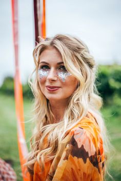 a woman with blue face paint standing in front of an orange and white pole, looking at the camera