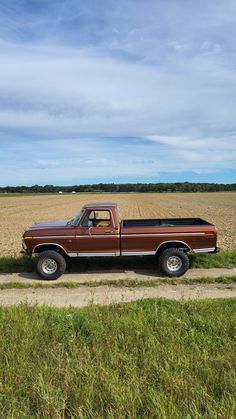 an old pickup truck is parked in the middle of a wheat field with blue sky and clouds