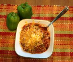 two green peppers sitting on top of a table next to a white bowl filled with chili and cheese