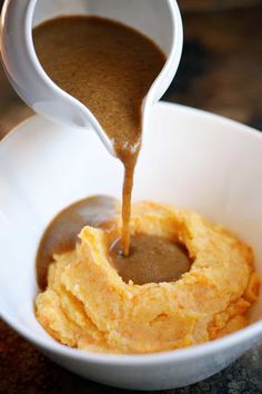 the sauce is being poured over the mashed potatoes in a white bowl with a spoon