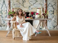 a woman sitting on a chair in front of a table with cakes and flowers behind her