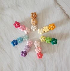 six small crocheted flowers are arranged in a circle on a white fur surface