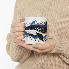 a woman holding a coffee mug with a whale painted on it