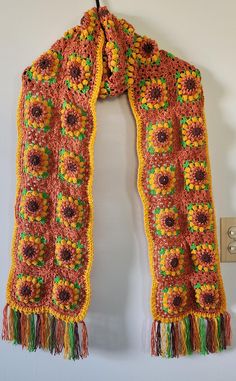 This beautiful, handmade crochet scarf features a vibrant sunflower design that brings warmth and cheer to any outfit. Crafted with meticulous care, the scarf showcases rich autumn colors, including earthy browns, golden yellows, and fresh greens, all arranged in intricate square motifs. Each sunflower is thoughtfully woven together, creating a striking pattern, while the playful multicolor tassels add a fun, bohemian touch. Soft and lightweight, this scarf is perfect for adding a pop of color and cozy texture to your wardrobe during the cooler months. Whether you wear it casually or for a special occasion, this unique accessory is sure to turn heads. Care: Hand wash recommended, lay flat to dry. Scarf Tying, Sunflower Design, Comfortable Fashion, Accessories Unique, Handmade Crochet, Crochet Scarf, Scarf Wrap, Fall Colors, Tassels