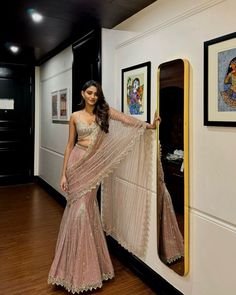 a woman standing next to a mirror in a room with pictures on the wall and wearing a sari