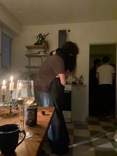 two people hugging each other in front of a table with wine glasses and candles on it