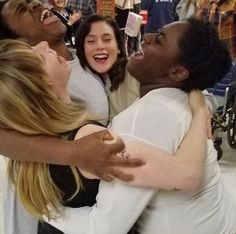 three women hugging each other in the middle of a room full of people and signs