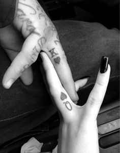 two people with tattoos on their fingers holding each other's hands and one has the word love written on it