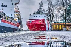 two large ships are docked next to each other in the water and one is red