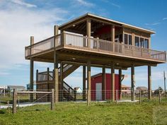 a house on stilts in the middle of a grassy area with a fence around it