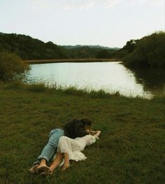 two people laying in the grass near a body of water