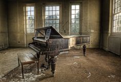 an old piano sitting in the middle of a room with broken windows and debris on the floor