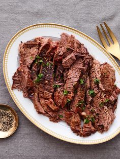 a white plate topped with sliced meat next to a bowl of seasoning and a fork