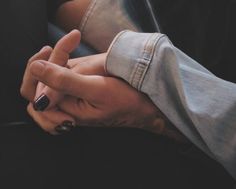 two hands holding each other while sitting on the ground in front of a car window