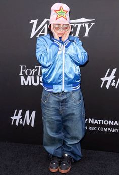 a young boy wearing jeans and a blue jacket with a star on it, standing in front of a black backdrop