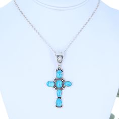 a silver cross with blue stones on a white mannequin neck piece, and a diamond necklace