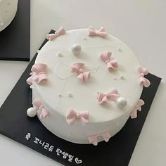 a white cake with pink bow decorations on it's side and black plate next to it