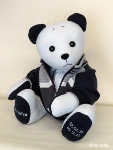 a white teddy bear wearing a black and gray jacket sitting on a white tablecloth