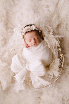 a newborn baby is wrapped in a white wrap and wearing a flower headband while laying on a fluffy blanket