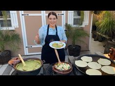 a woman in an apron is holding a plate with guacamole and tortillas on it