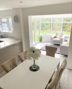 a kitchen table with chairs and a clock on the wall in front of it that is next to a living room