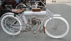 an old fashioned bicycle is parked on the pavement in front of other antique motorcycles and people