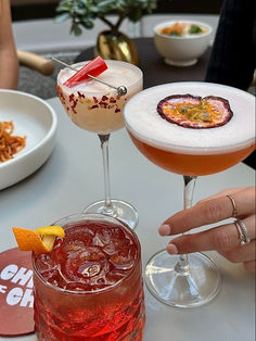 two cocktails are sitting on a table next to plates and bowls with condiments