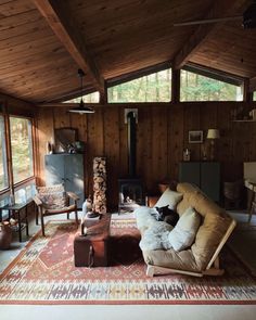 a living room with wood paneling and lots of windows on the wall, couches and chairs in front of an open fire place