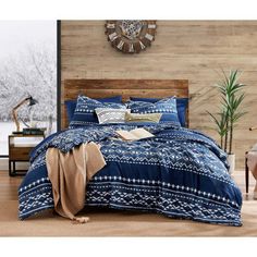 a bed with blue and white comforter in front of a wooden headboard next to a clock