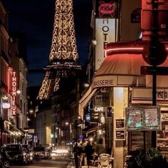 the eiffel tower is lit up at night in paris, france as people walk down the street